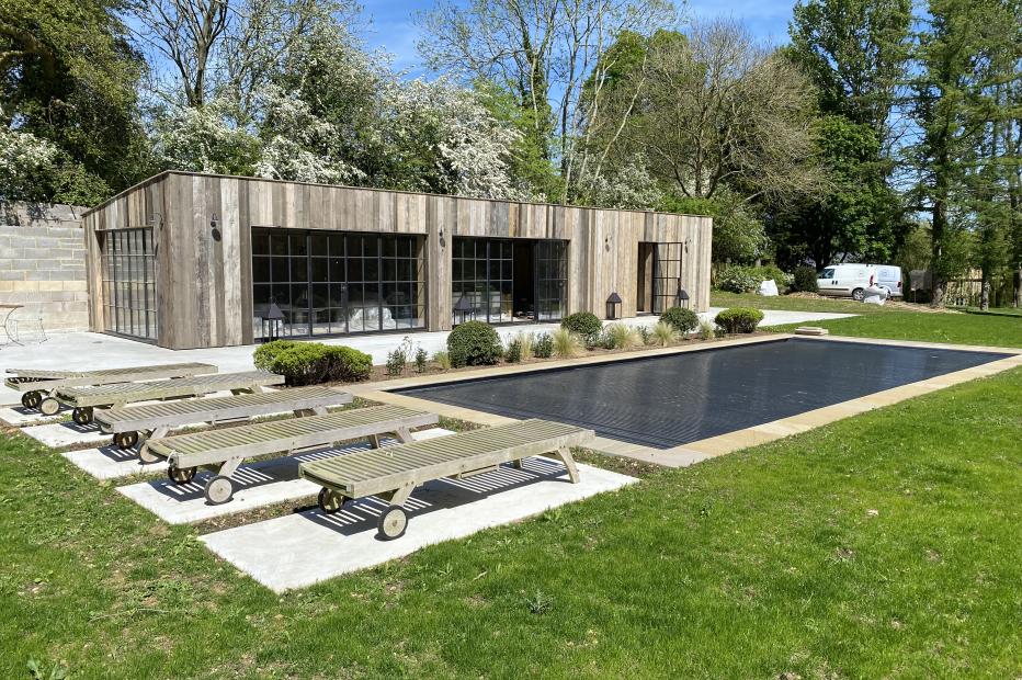 pool house with pool and decking chairs in a garden 